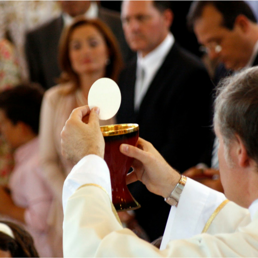 Padre ergue a eucaristia em Missa