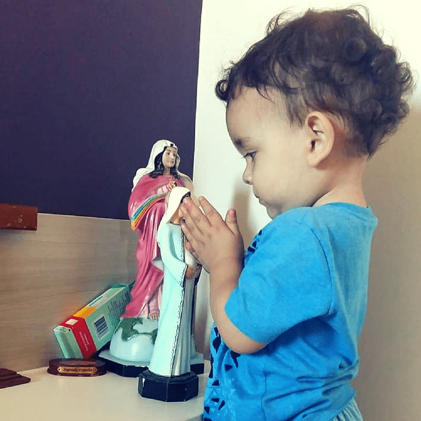 Criança ora em frente a imagem de Maria