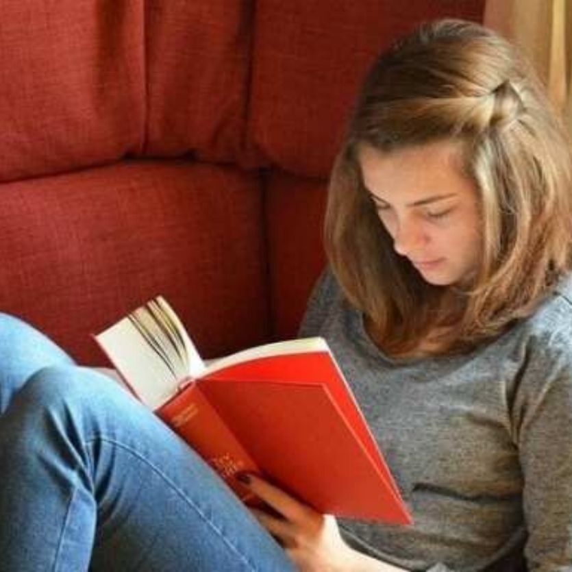 garota-loira-sentada-no-sofá-vermelho-lê-livro