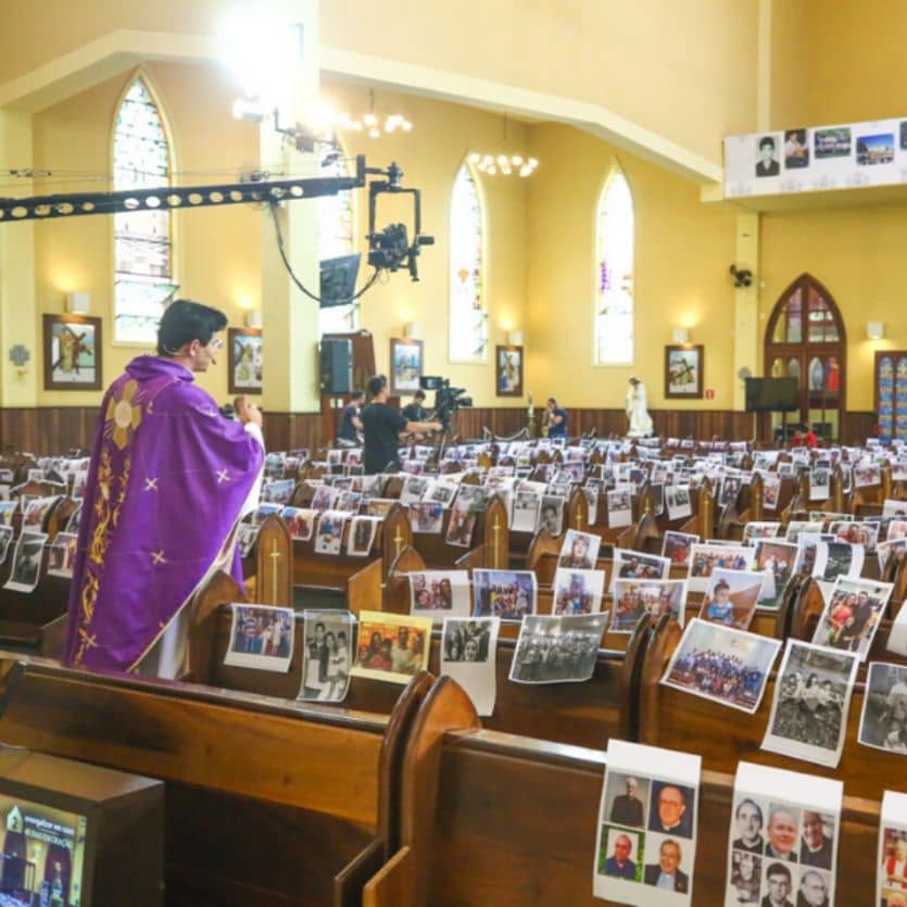 Padre celebra numa igreja cheia de fotos dos fiéis