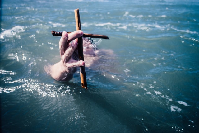 Homem submerso segura uma cruz sobre as águas